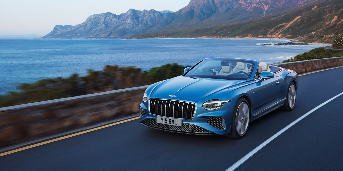 Thomas Exclusive Cars GmbH New Bentley Continental GTC Azure convertible in Light Windsor blue paint with 22 inch Azure wheels and chrome grill, driving dynamically by the sea