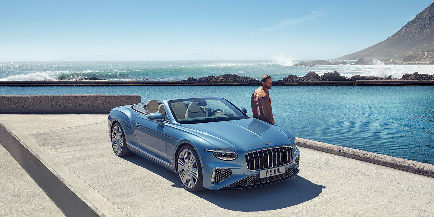 Thomas Exclusive Cars GmbH New Bentley Continental GTC Azure convertible front view in Light Windsor blue paint with 22 inch ten spoke wheels parked by the sea in the sunshine