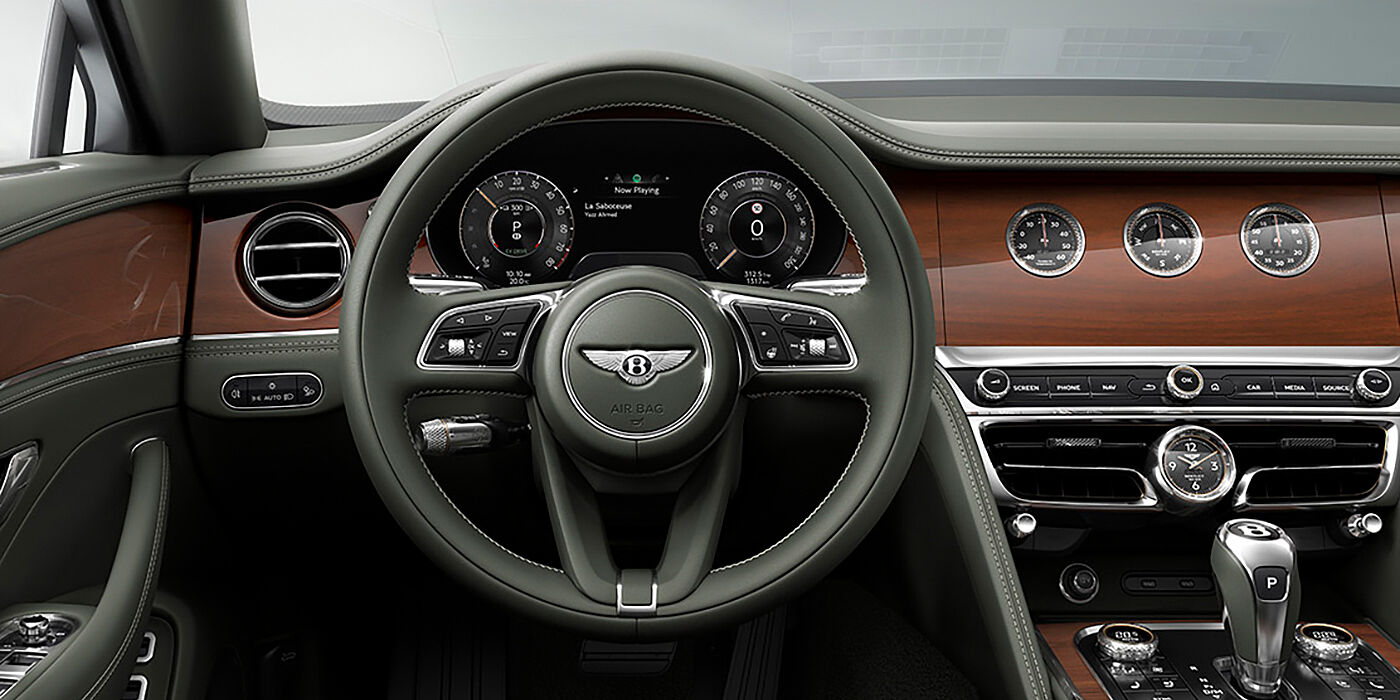 Thomas Exclusive Cars GmbH New Bentley Flying Spur sedan front cabin in Cumbrian Green hide and Crown Cut walnut veneer showing steering wheel and Rotating Display with three clocks on face