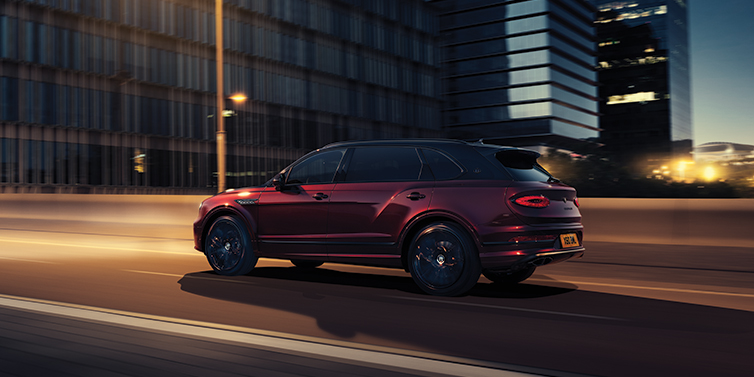 Thomas Exclusive Cars GmbH Bentley Bentayga Extended Wheelbase Mulliner SUV in Cricket Ball red paint driving dynamically in city at night