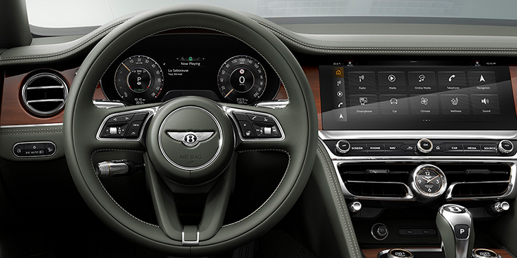 Thomas Exclusive Cars GmbH New Bentley Flying Spur front cabin interior in Cumbrian green hide with Crown Cut walnut veneer showing steering wheel and driver controls